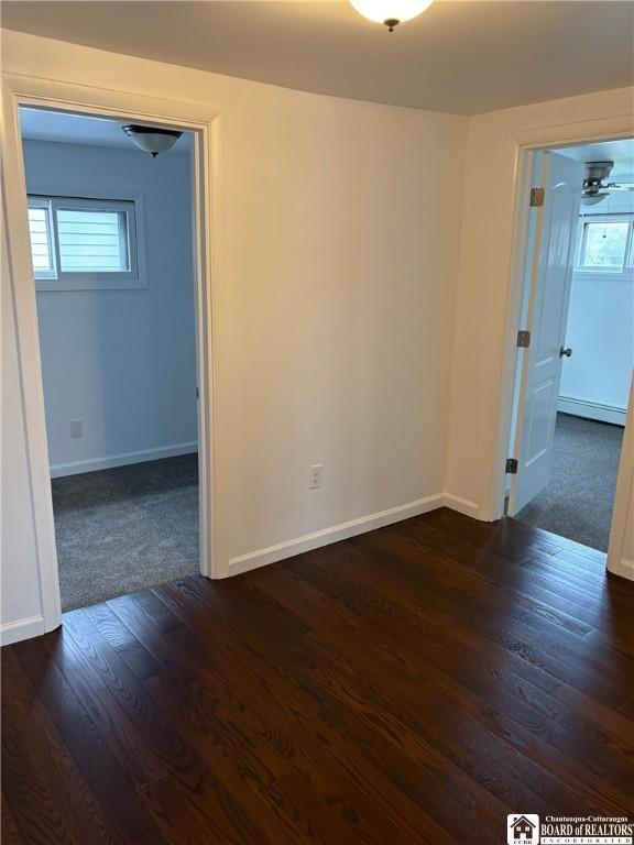 unfurnished room featuring baseboards, a baseboard heating unit, and dark wood-type flooring