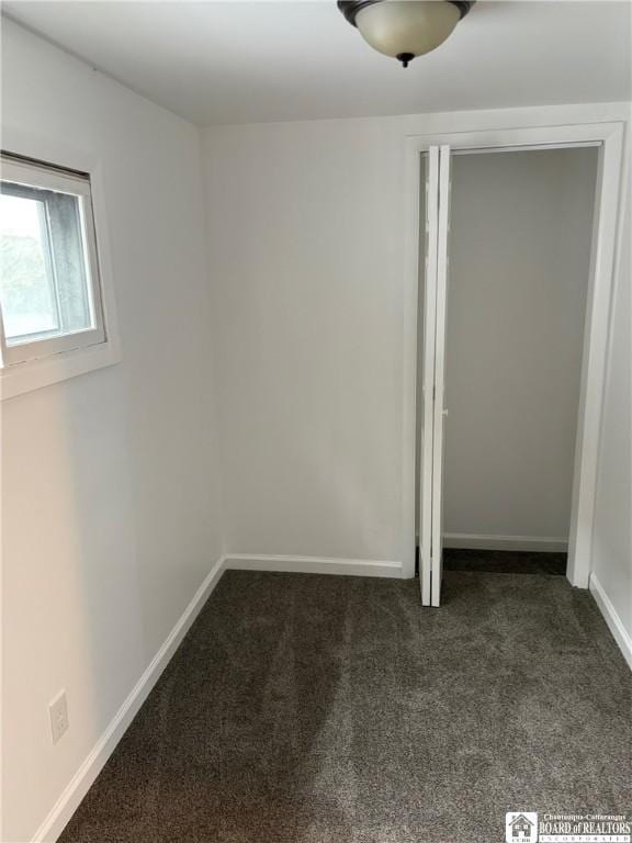 unfurnished bedroom with dark carpet, baseboards, and a closet
