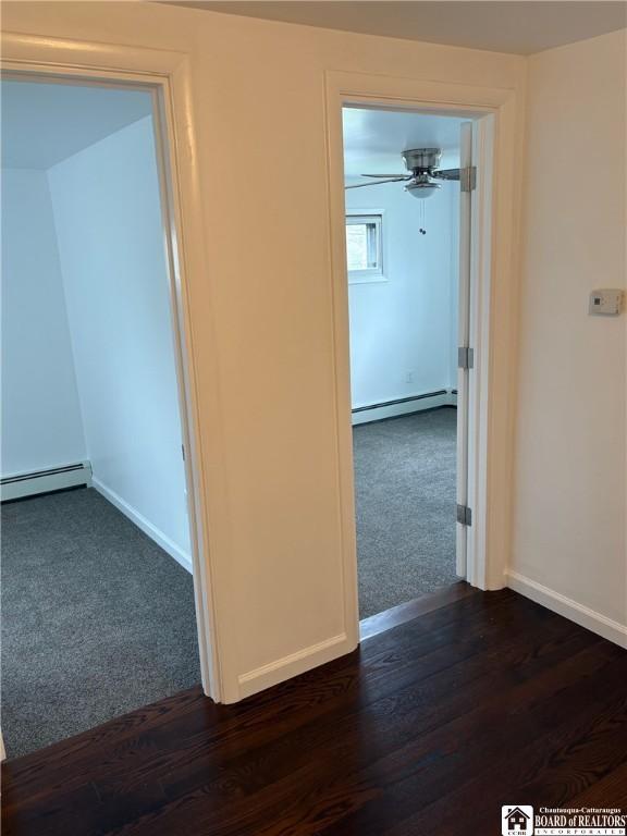 hallway with dark wood finished floors, baseboards, a baseboard radiator, a baseboard heating unit, and dark carpet