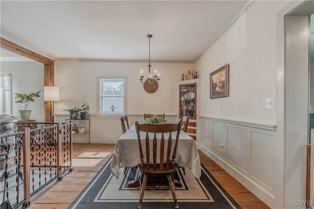 dining space featuring light wood-style floors, crown molding, a wainscoted wall, and an inviting chandelier