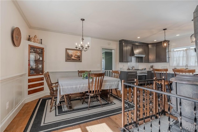 dining area featuring ornamental molding, wainscoting, light wood-type flooring, and a notable chandelier