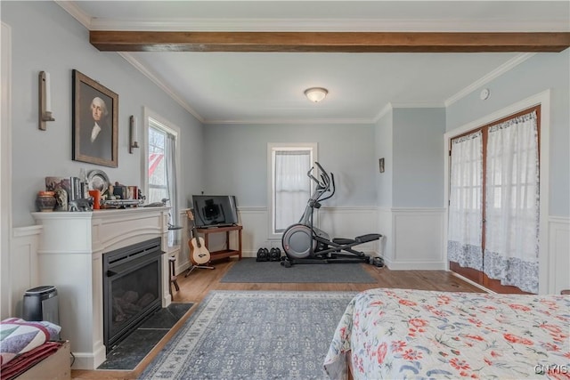 bedroom with a fireplace with flush hearth, ornamental molding, wood finished floors, and a wainscoted wall