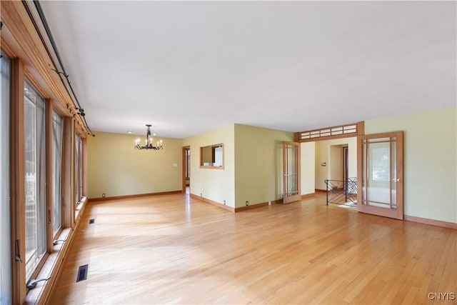 spare room with baseboards, a notable chandelier, a healthy amount of sunlight, and light wood-type flooring
