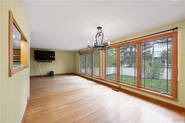 unfurnished dining area with baseboards, a chandelier, wood finished floors, and visible vents