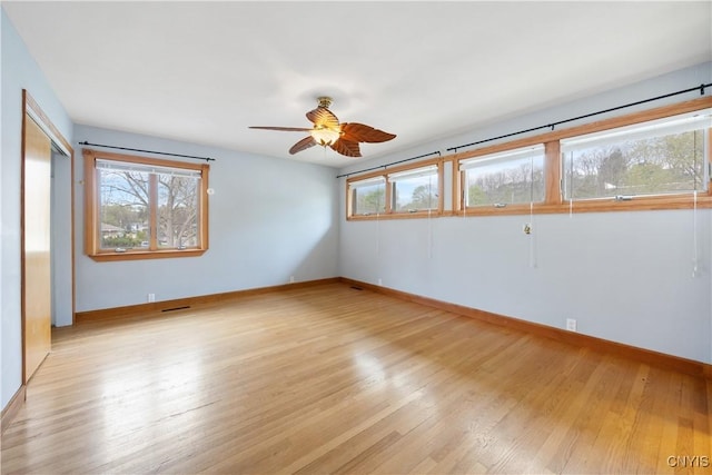 empty room with baseboards, a ceiling fan, light wood-style flooring, and a wealth of natural light