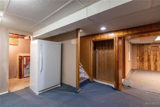 finished below grade area featuring freestanding refrigerator, carpet, wood walls, and stairway