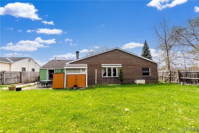 back of property featuring brick siding, a fenced backyard, a lawn, and a storage unit