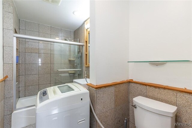 full bathroom featuring wainscoting, a sink, toilet, washer / clothes dryer, and tile walls