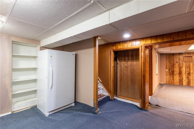 finished basement featuring carpet, stairway, freestanding refrigerator, and wood walls
