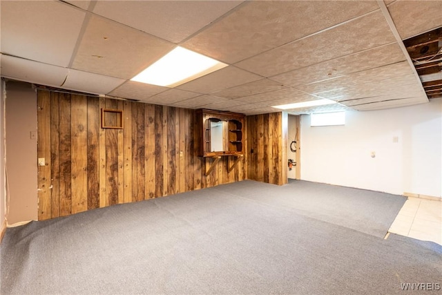 basement featuring carpet floors, wood walls, and a drop ceiling