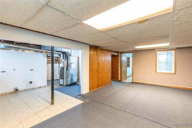 basement featuring heating unit, wooden walls, and a paneled ceiling