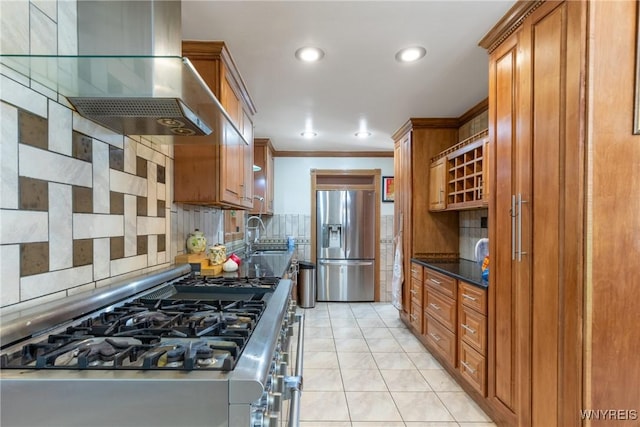 kitchen with brown cabinetry, wall chimney exhaust hood, backsplash, and stainless steel appliances