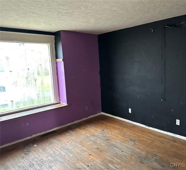 empty room with wood-type flooring, a textured ceiling, and baseboards