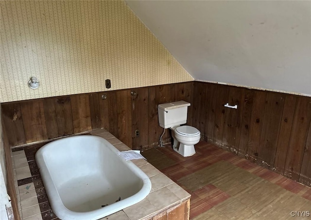 full bathroom featuring wainscoting, toilet, wallpapered walls, wood finished floors, and a tub to relax in
