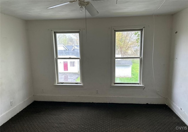 empty room with dark carpet, a ceiling fan, and baseboards