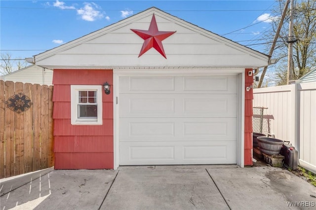 detached garage featuring concrete driveway and fence
