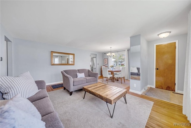 living room with an inviting chandelier, light wood finished floors, baseboards, and visible vents