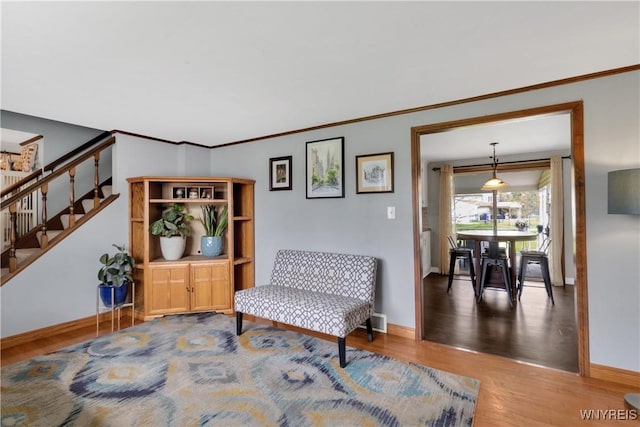 sitting room featuring stairway, baseboards, crown molding, and wood finished floors