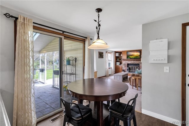 dining space with baseboards, a brick fireplace, wood finished floors, and visible vents