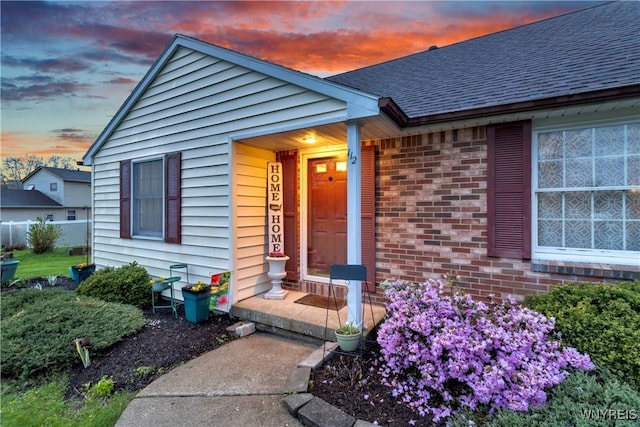 view of exterior entry featuring brick siding and a shingled roof