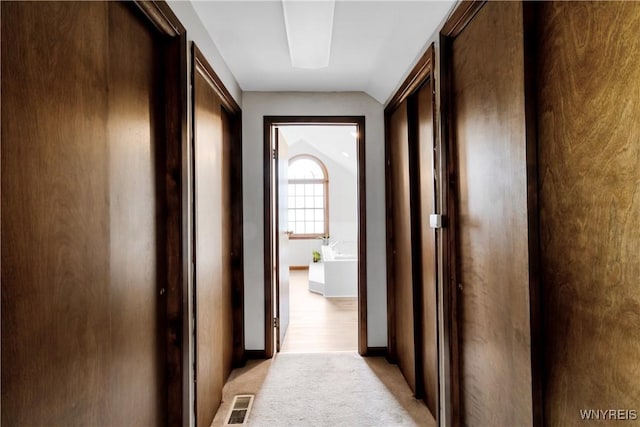 hall featuring light colored carpet, baseboards, lofted ceiling, and visible vents