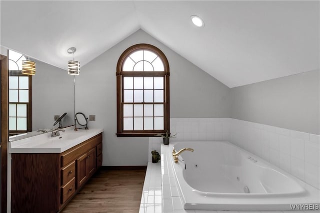 full bath featuring a tub with jets, wood finished floors, vanity, baseboards, and lofted ceiling