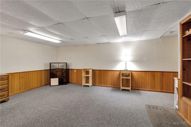 miscellaneous room with wooden walls, a wainscoted wall, carpet, and a drop ceiling