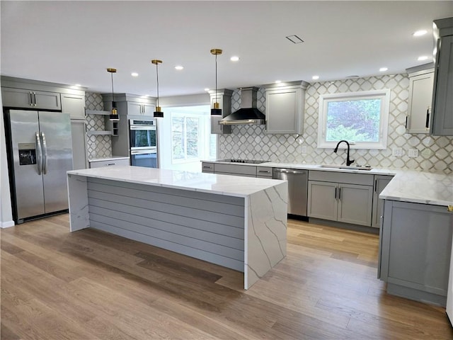 kitchen featuring wall chimney range hood, decorative backsplash, gray cabinetry, a sink, and stainless steel appliances