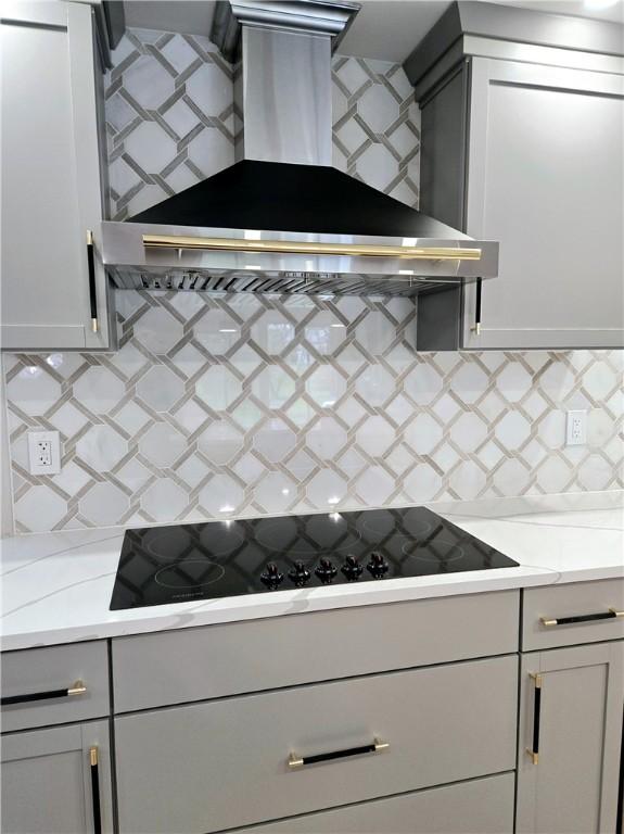 kitchen featuring wall chimney range hood, black electric cooktop, decorative backsplash, and light countertops