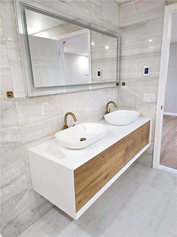 bathroom with double vanity, tile walls, a sink, and tasteful backsplash