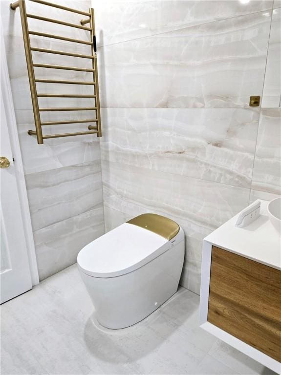 half bathroom with tile walls, vanity, toilet, marble finish floor, and radiator heating unit