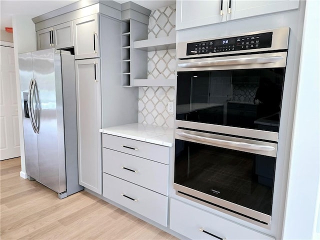 kitchen featuring open shelves, light stone countertops, light wood-type flooring, appliances with stainless steel finishes, and backsplash