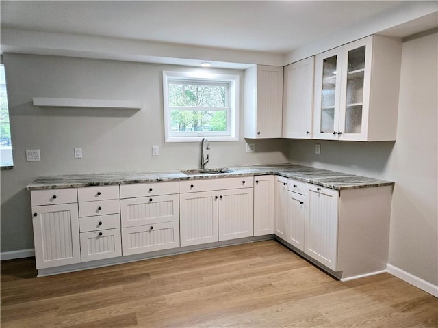 kitchen featuring light stone counters, a sink, white cabinetry, baseboards, and light wood-type flooring