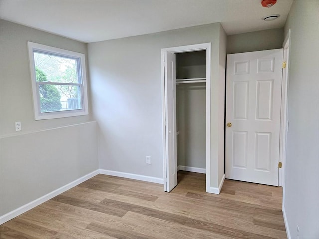unfurnished bedroom featuring light wood-style floors, baseboards, and a closet
