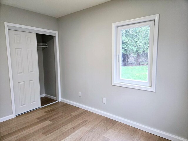 unfurnished bedroom with baseboards, light wood-style flooring, and a closet