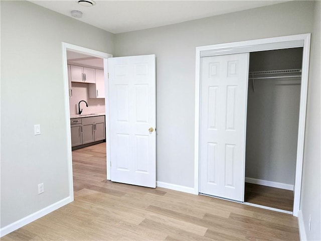 unfurnished bedroom with a sink, baseboards, and light wood finished floors