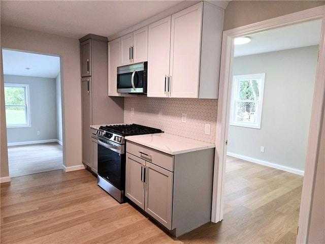 kitchen featuring light wood-style floors, gray cabinets, backsplash, and stainless steel appliances