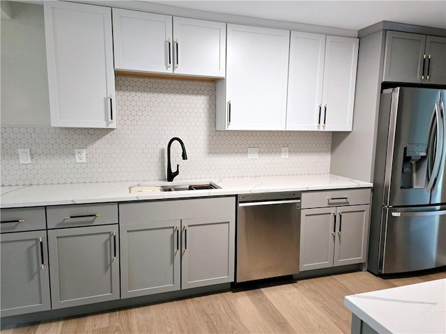 kitchen featuring light wood-type flooring, light stone counters, a sink, gray cabinetry, and stainless steel appliances