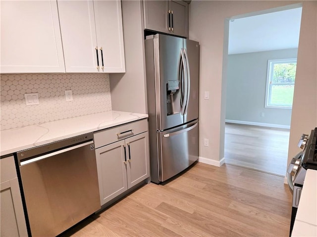 kitchen featuring backsplash, light stone counters, baseboards, light wood finished floors, and stainless steel appliances