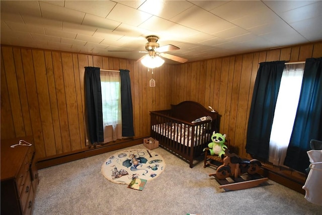 bedroom featuring a ceiling fan, wood walls, a baseboard heating unit, and carpet