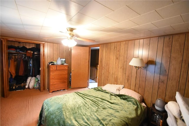 carpeted bedroom featuring a closet, a ceiling fan, and wooden walls