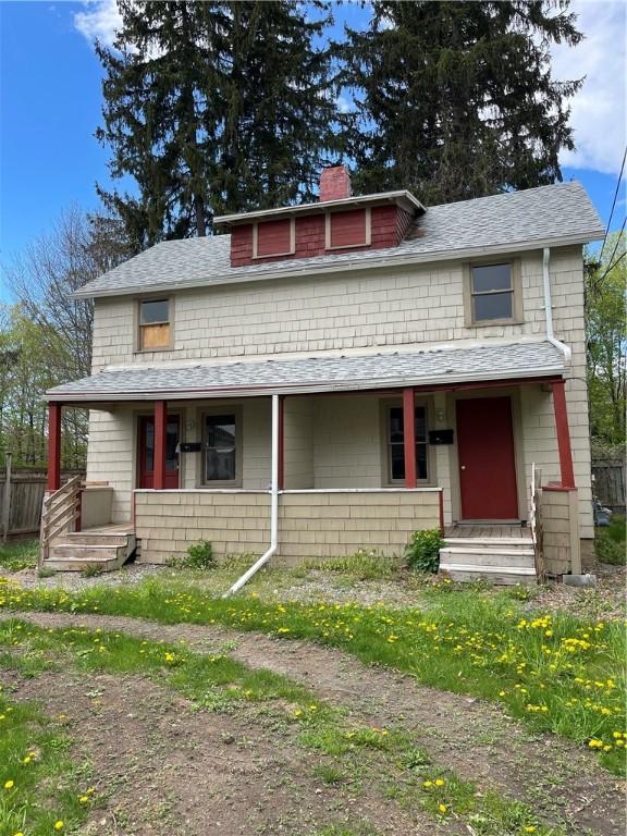 view of front of house with a porch, a shingled roof, fence, and a chimney