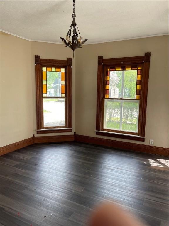 unfurnished room featuring baseboards, ornamental molding, dark wood-type flooring, and an inviting chandelier