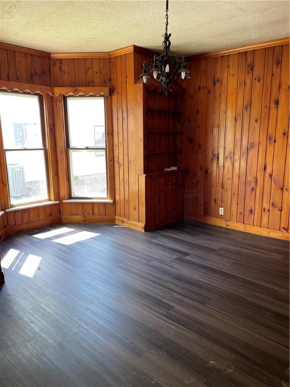 unfurnished dining area with wooden walls, baseboards, dark wood-style flooring, and a chandelier