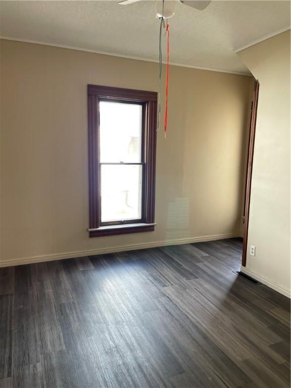 unfurnished room with dark wood-type flooring, a ceiling fan, baseboards, and crown molding