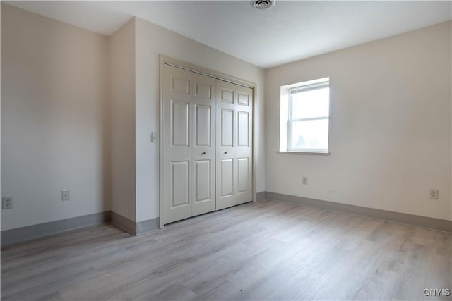 unfurnished bedroom featuring baseboards, a closet, light wood finished floors, and visible vents