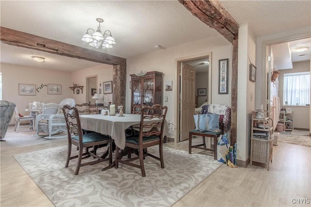 dining room with light wood-style floors, an inviting chandelier, and beamed ceiling