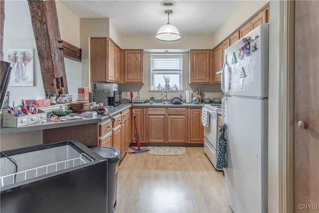 kitchen with brown cabinets, a sink, white appliances, light wood-style flooring, and pendant lighting