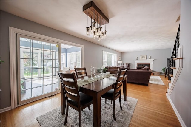 dining area with visible vents, stairs, a fireplace, baseboards, and light wood finished floors