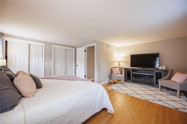 bedroom featuring baseboards, light wood-style flooring, two closets, and visible vents